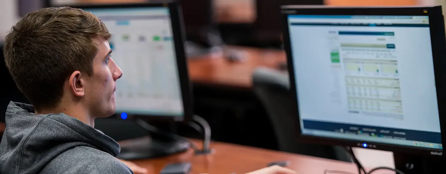 A male student sitting at a desk in front of a computer screen.